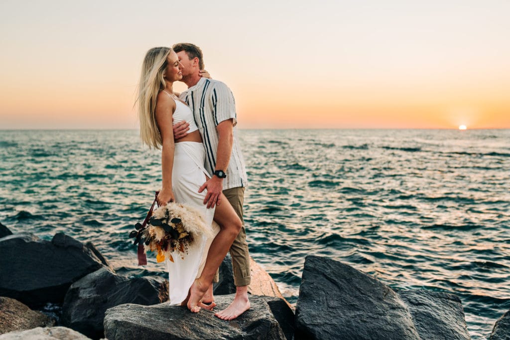 Elopement Photographer, bride and groom kiss on rocks before the ocean at sunset