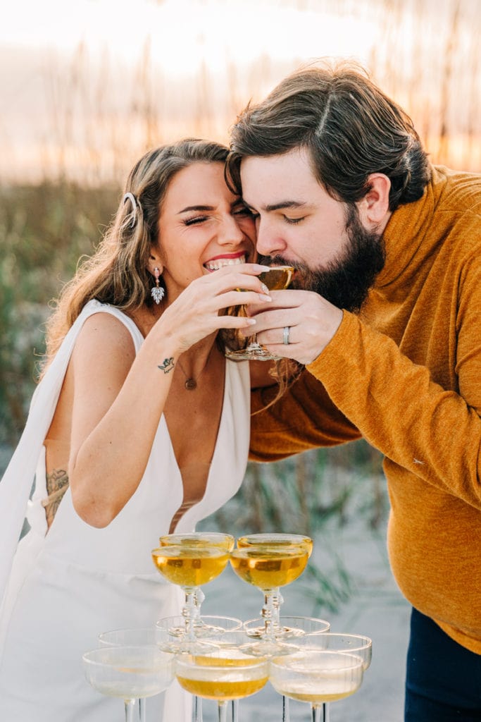 Wedding Photographer, the bride and groom share a glass of champagne, sipping together, she laughs
