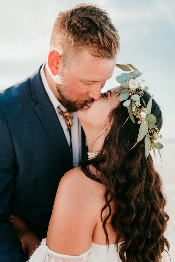 Elopement Photographer, bride and groom kiss at the beach, she wears a floral crown