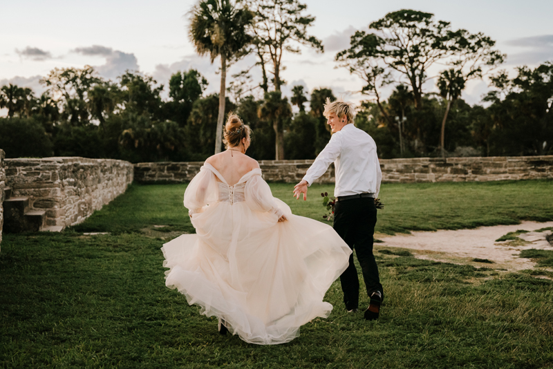 Wedding Photographer, Groom reaches for brides hands as they walk through the grass