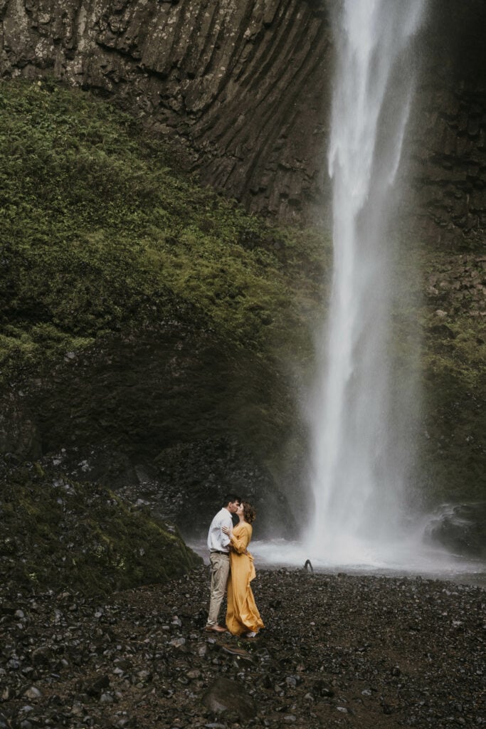 Couple stands at the base of a waterfall in Oregon kissing.