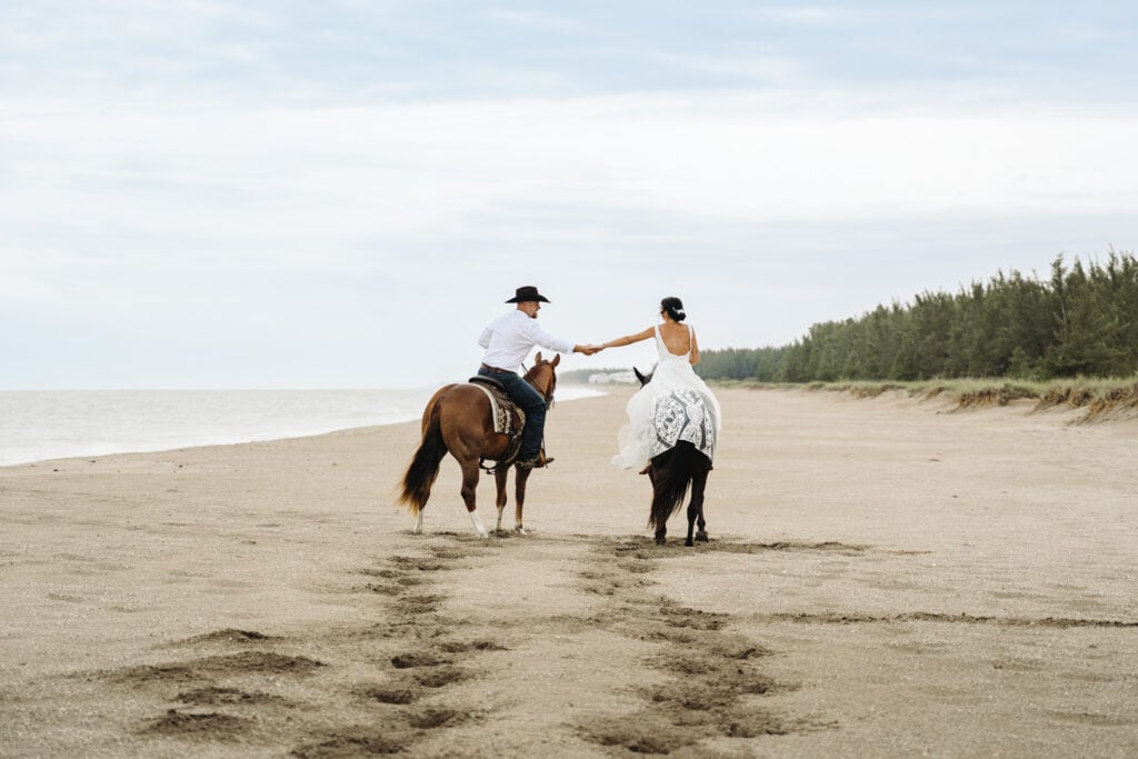 bride and groom ride horses on the beach at sunrise