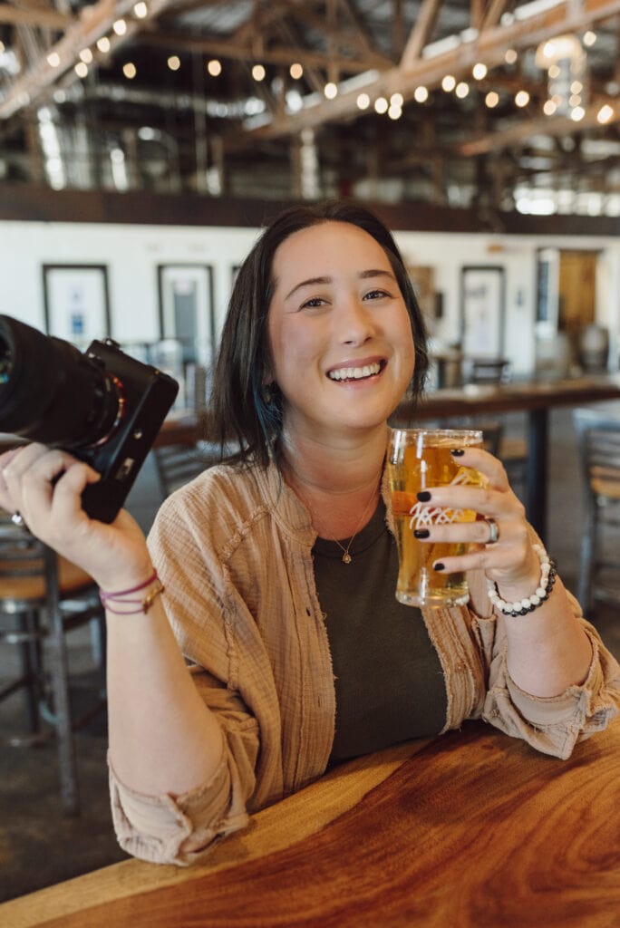 Wedding Photographer, Jessica Lauren, holds her camera as she sits in a brewery holding a drink