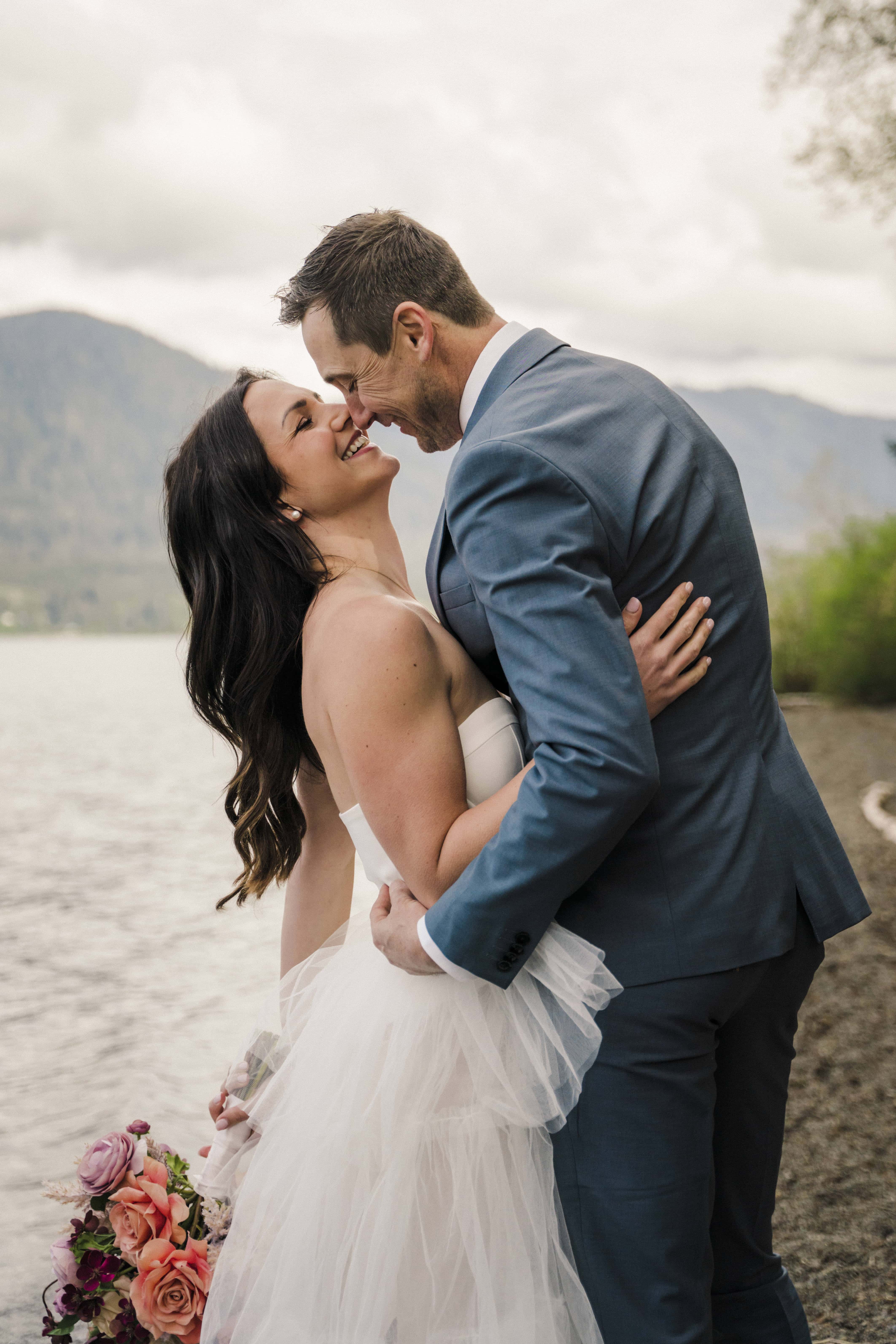 bride and groom stand at edge of alpine lake in washington