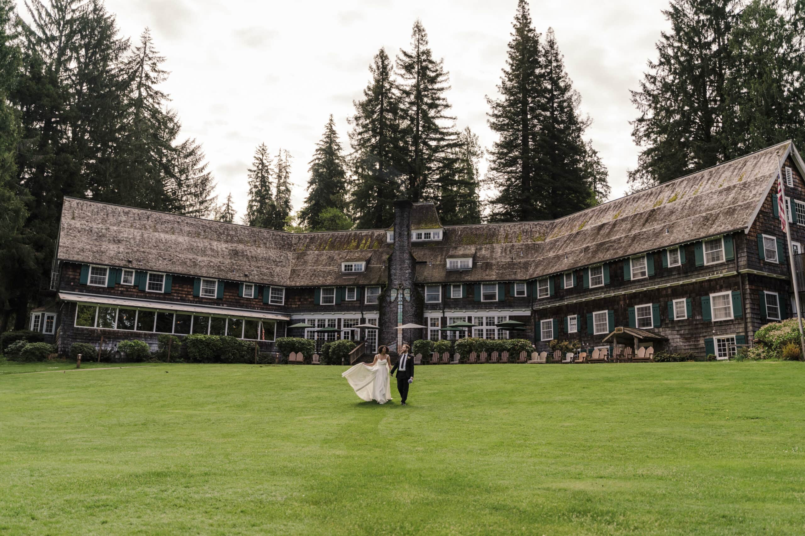 couple walks in front of the lake quinault lodge in their wedding clothes