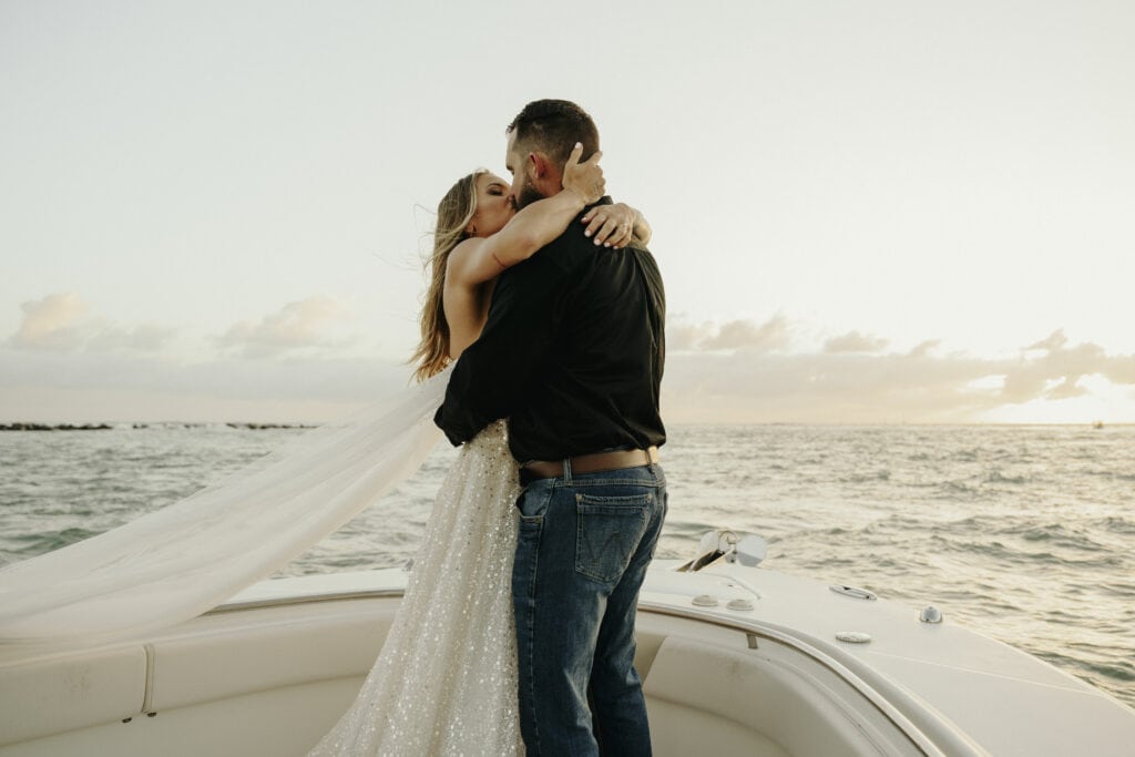 a couple kisses after saying "I do" on a boat at sunrise